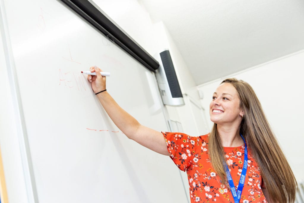 Studio Cambridge teacher smiles as she writes on a white board in a lesson.