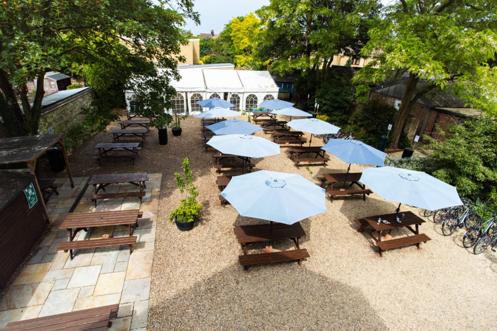 Tables and umbrellas on a sunny day in the Studio Cambridge garden.