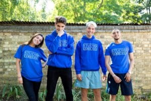 Welfare team at Sir Michael English summer camp smile and pose for camera against wall of Studio Cambridge main school garden