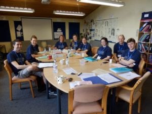 The welfare team at Sir Edward residential English summer camp sit around a table at a meeting, smiling