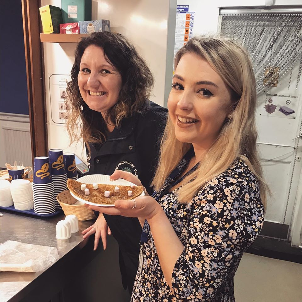 Stephanie and Siobhan, two members of staff at Studio Cambridge, smile whilst holding a plate with a pancake topped with marshmallows. Pancakes were made to celebrate pancake day with our international English students.
